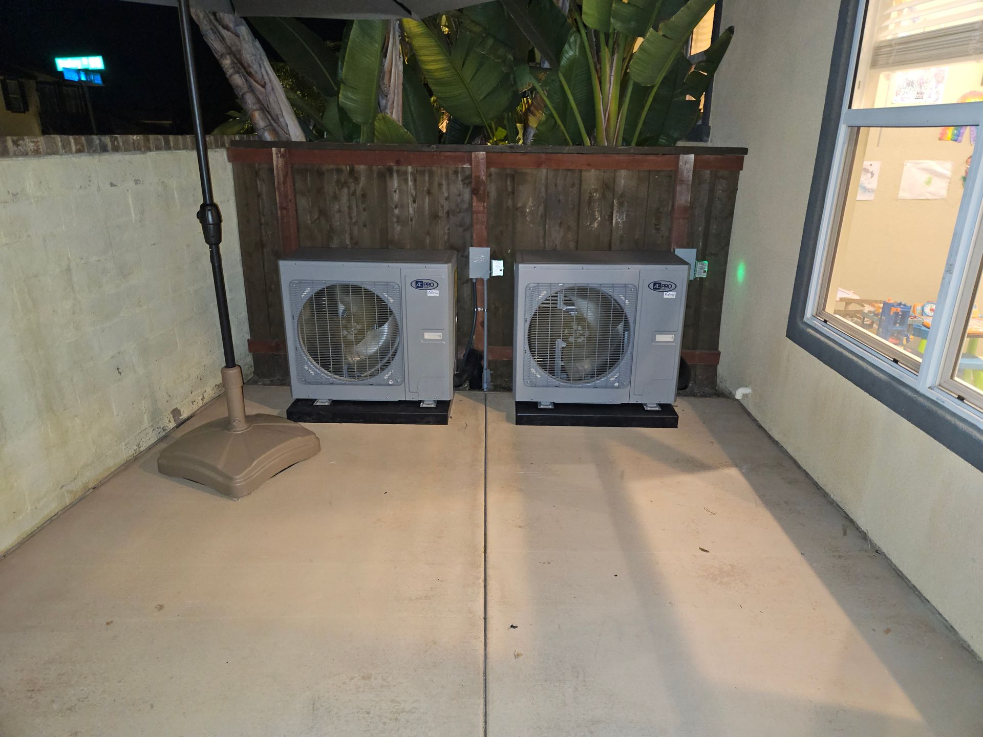 Two air conditioners are sitting on a patio next to a window.