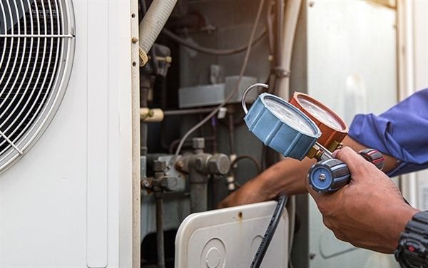 A man is working on an air conditioner with a pressure gauge.