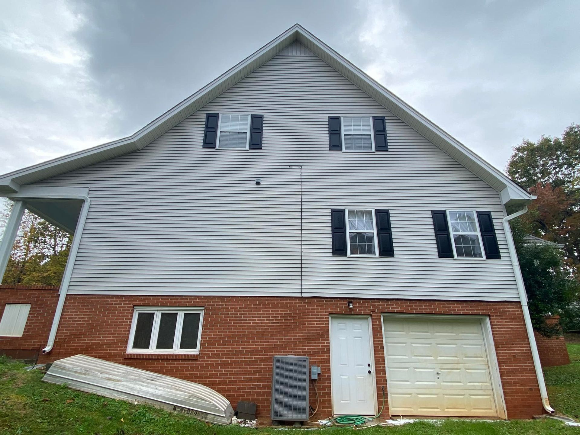 A large white house with black shutters is sitting on top of a grassy hill.