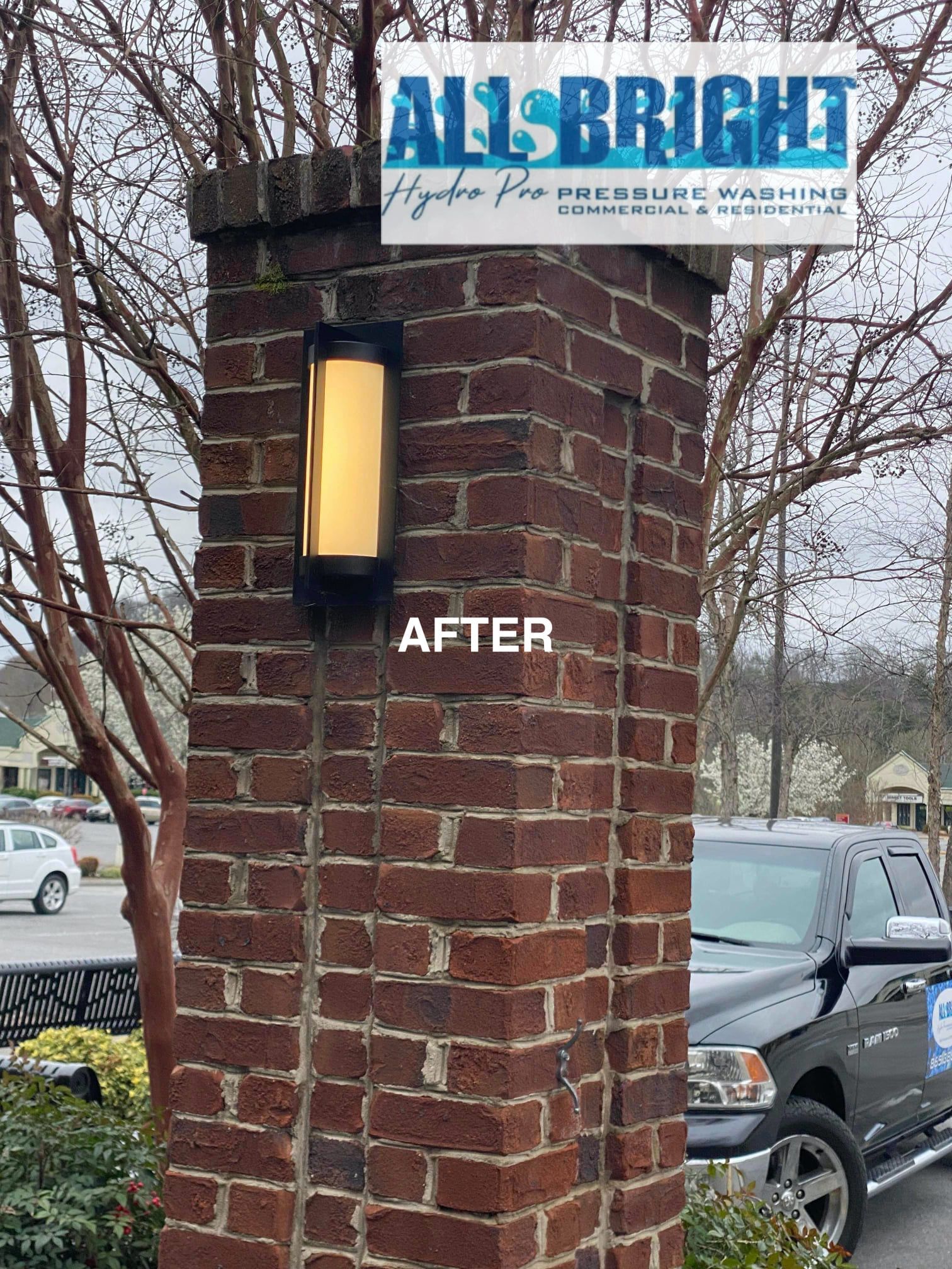 A brick pillar with a light on it and a truck parked in front of it.