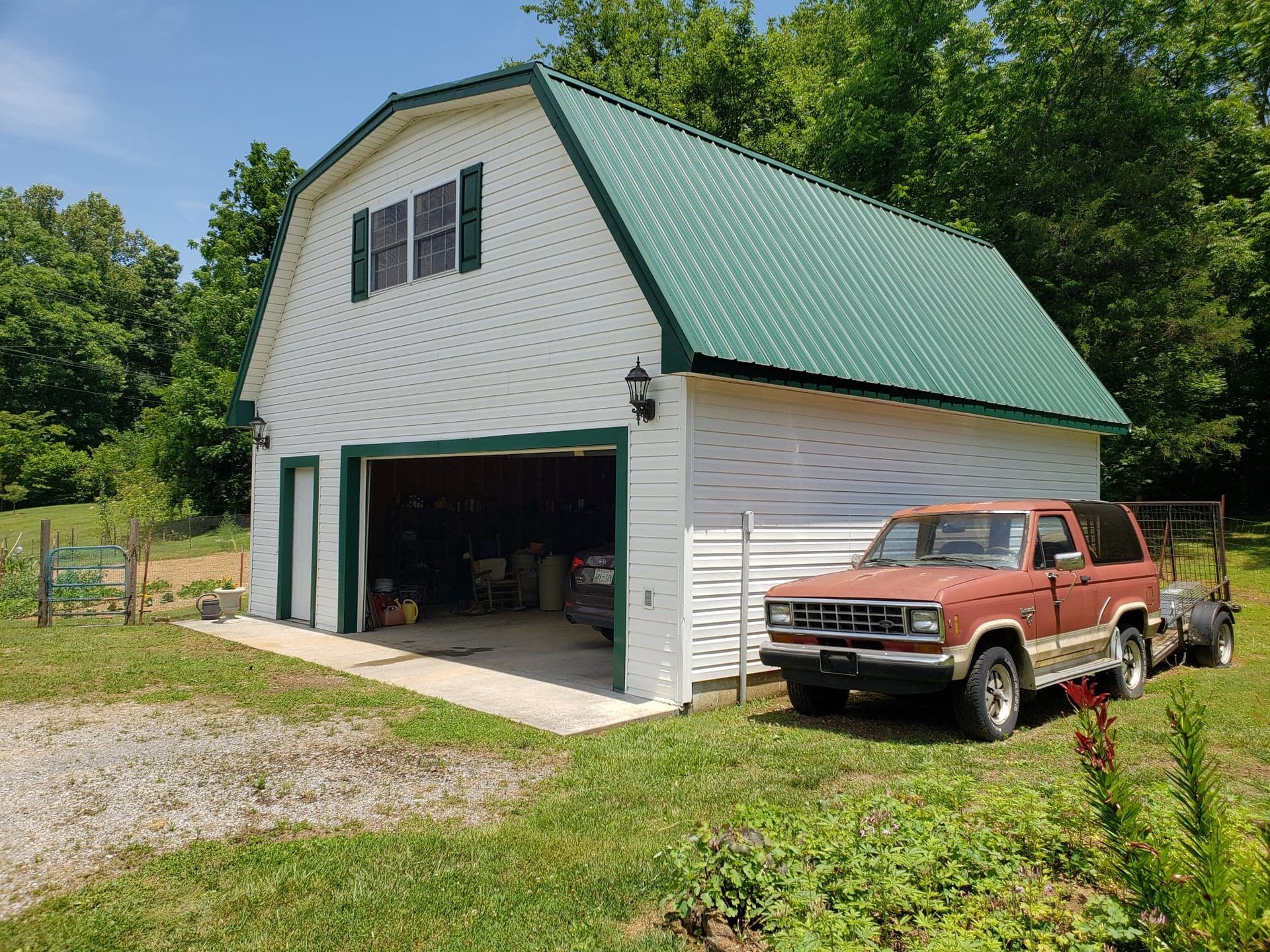A red truck is parked in front of a white barn with a green roof.