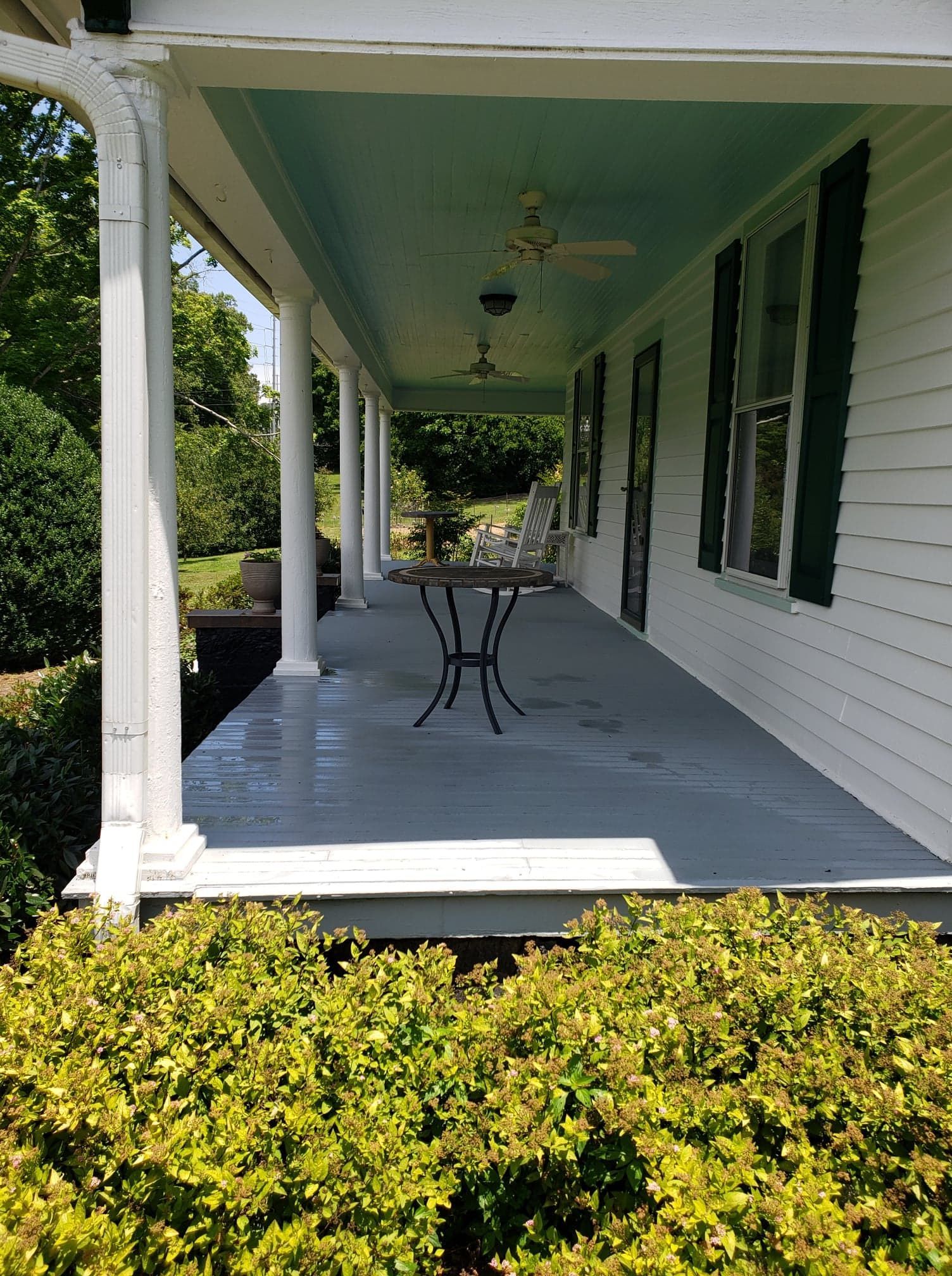 A porch with a table and chairs on it and a ceiling fan.