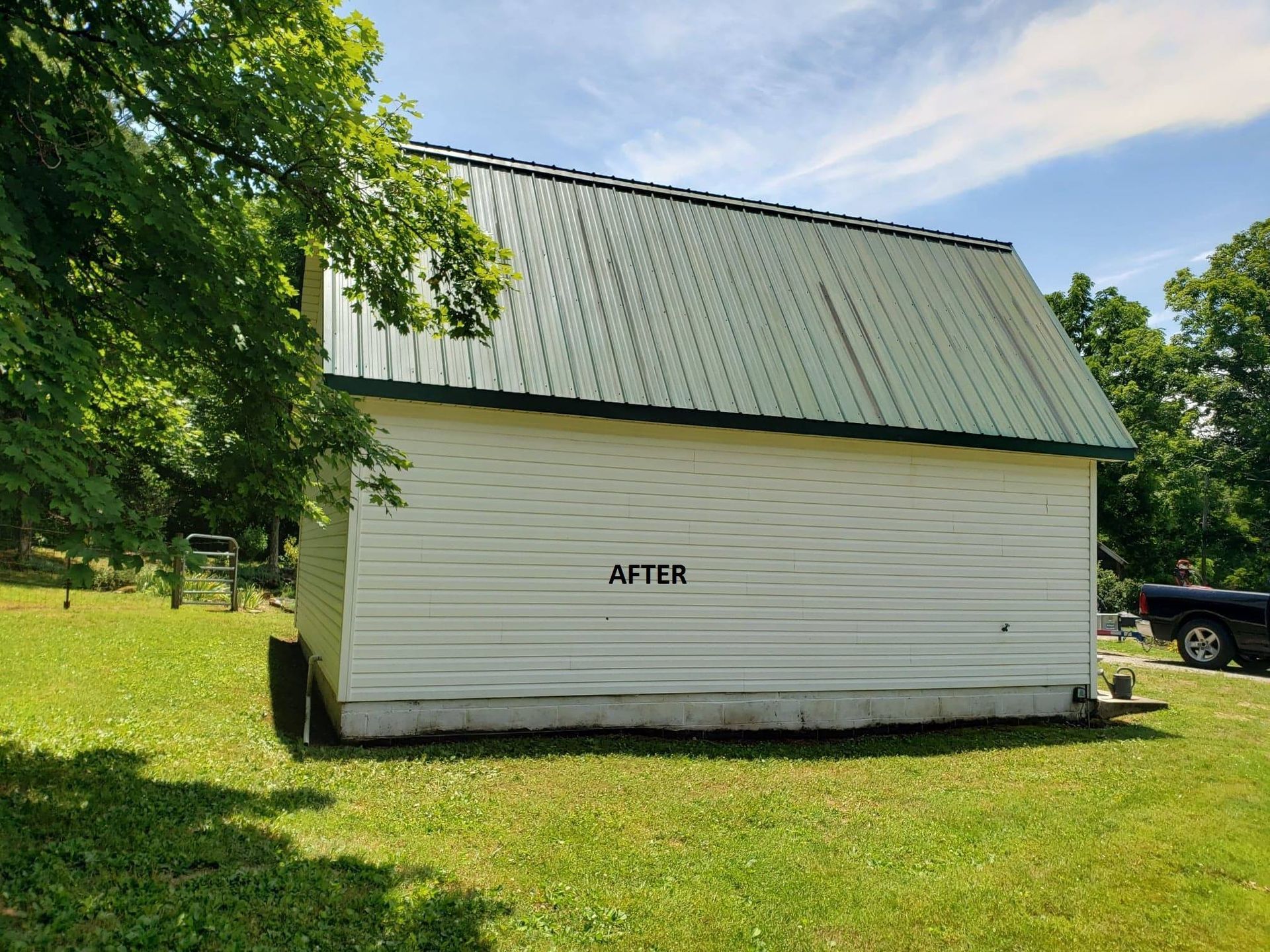 A white barn with a green roof is sitting in the middle of a grassy field.
