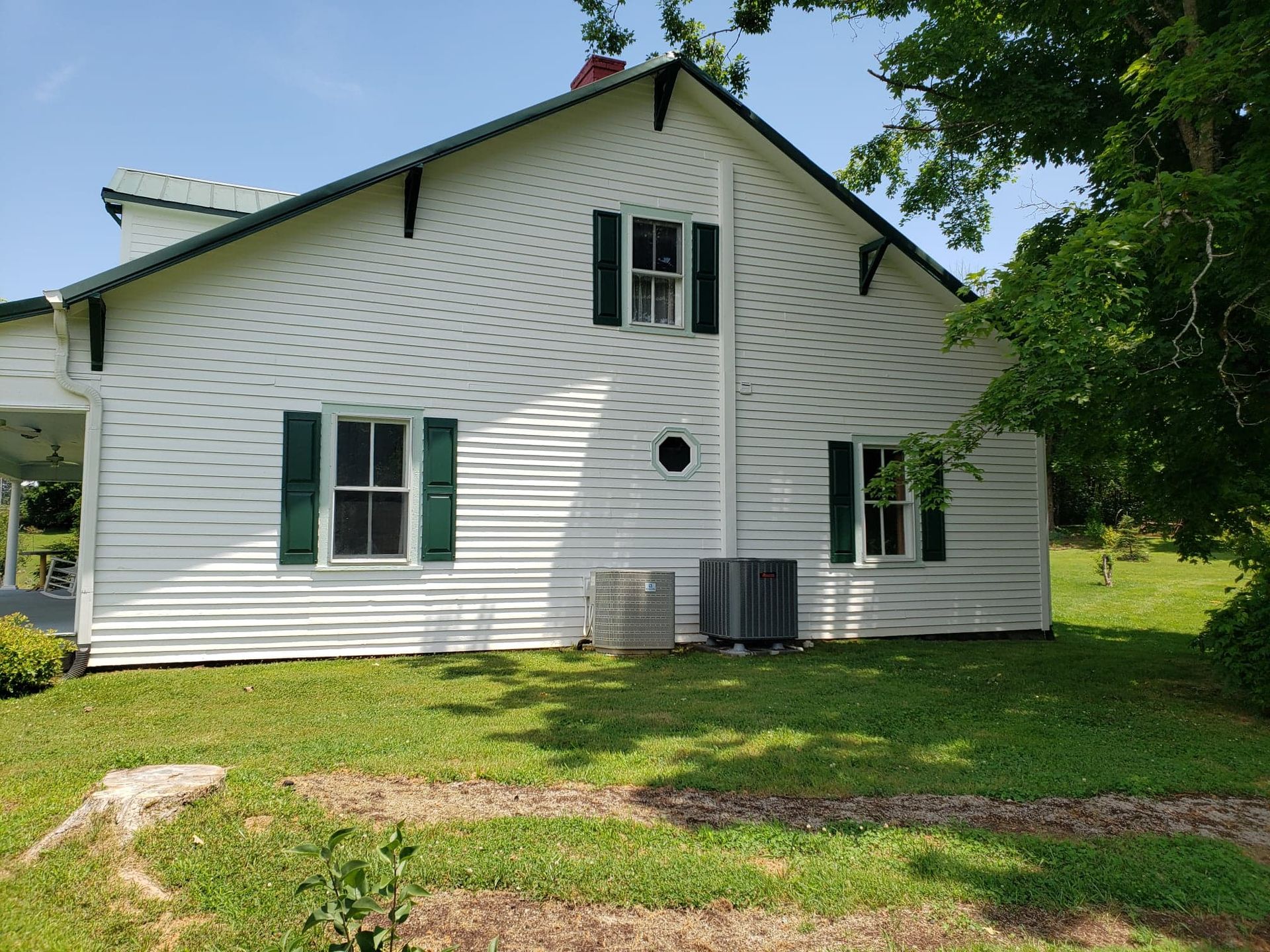 A white house with green shutters is sitting on top of a lush green field.