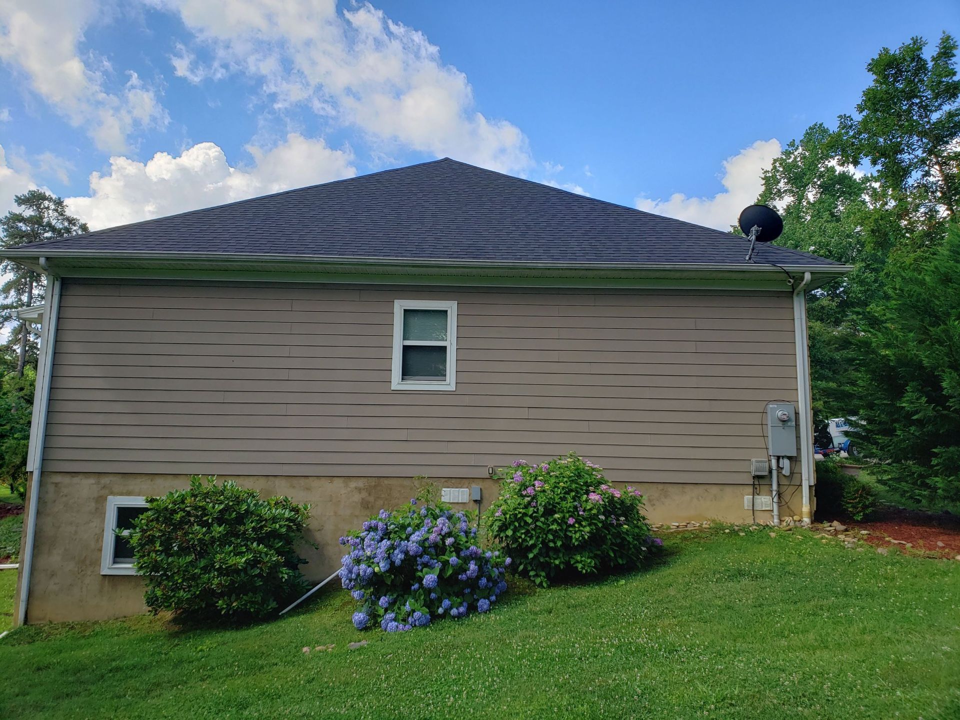 A house with a roof that is covered in shingles is sitting on top of a lush green hillside.