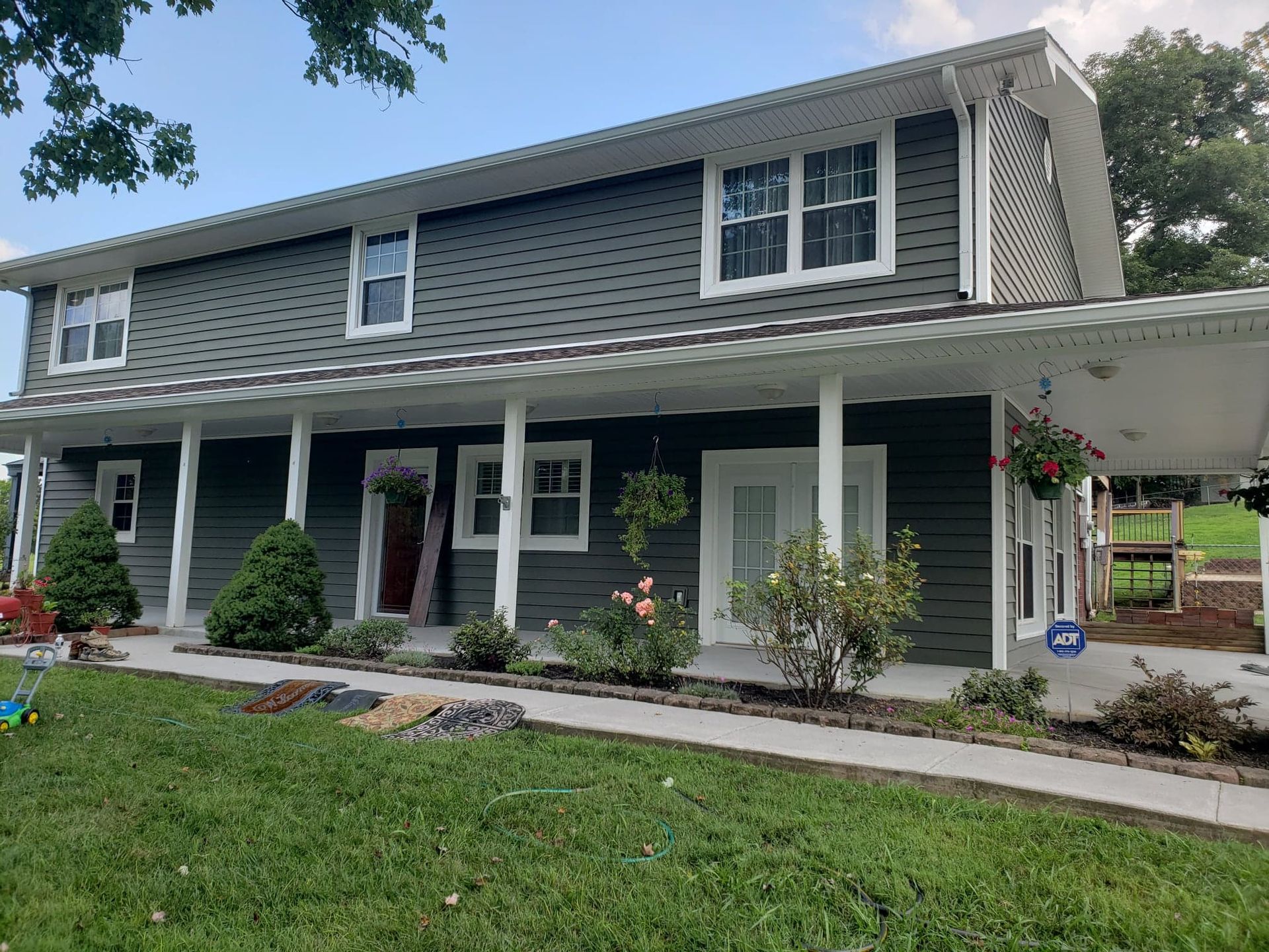 A large house with a large porch is sitting on top of a lush green field.