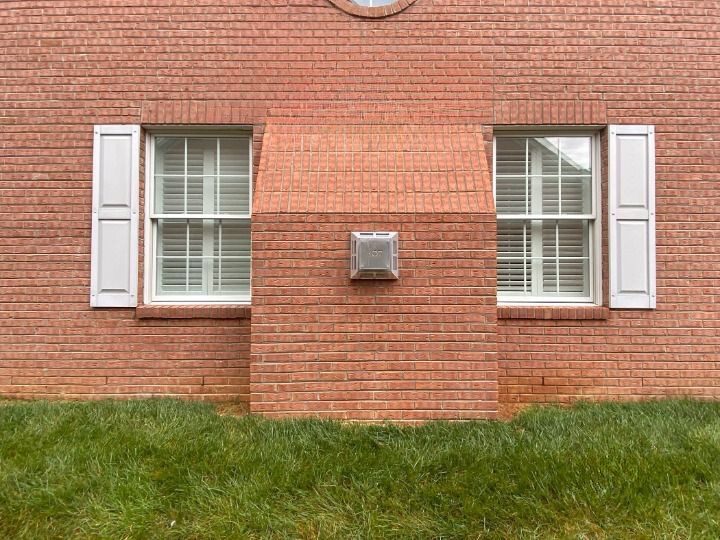 A red brick building with two windows and white shutters.