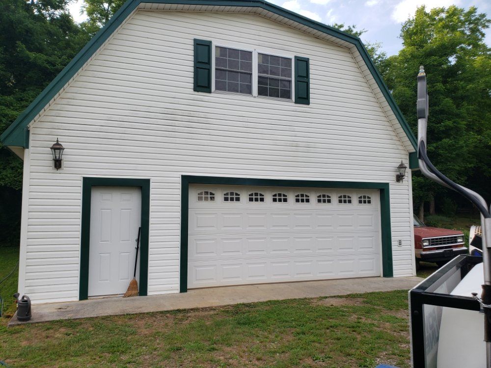 A white garage with green shutters and a red truck parked in front of it.
