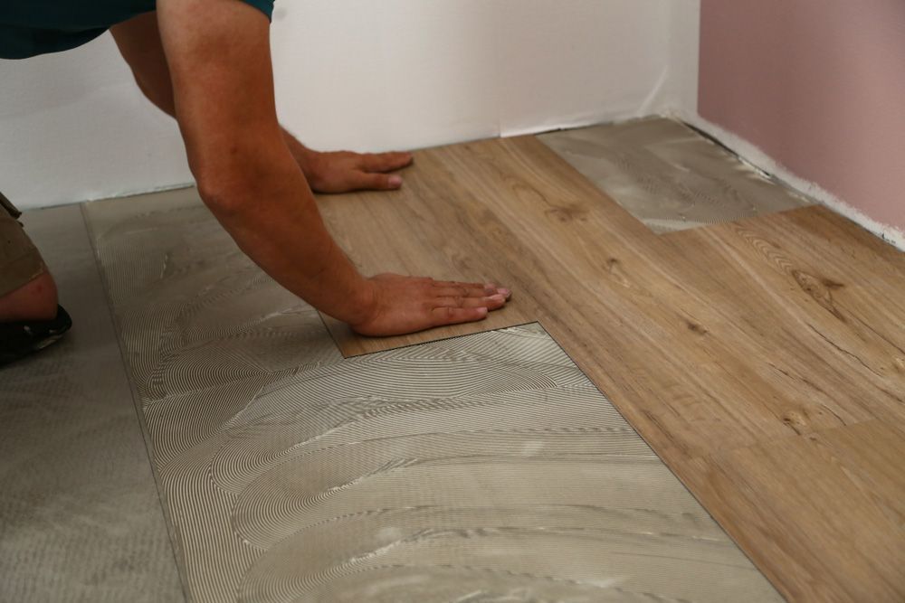 A Man Is Installing A Wooden Floor In A Room — Affordable Carpets Woolgoolga In Woolgoolga, NSW