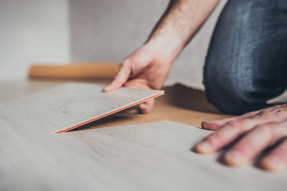 A Person Is Laying A Piece Of Vinyl Flooring On The Floor — Affordable Carpets Woolgoolga In Coffs Harbour, NSW