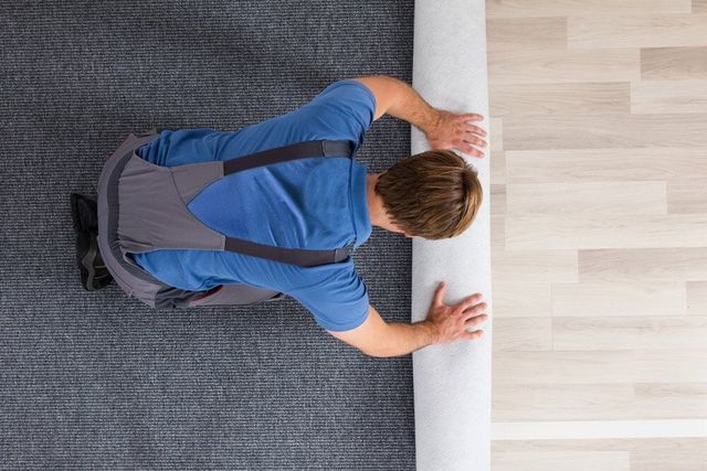 A Man Is Rolling A Carpet On The Floor — Affordable Carpets Woolgoolga In Woolgoolga, NSW
