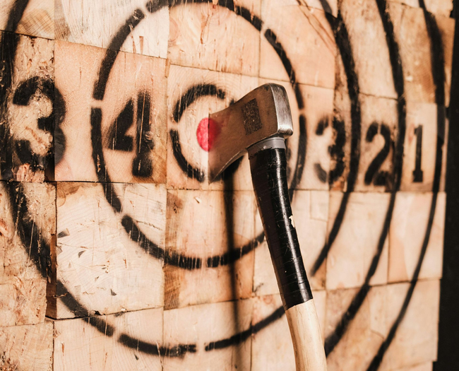 A metal axe embedded in the center of a wooden target board marked with numbers in concentric circles.