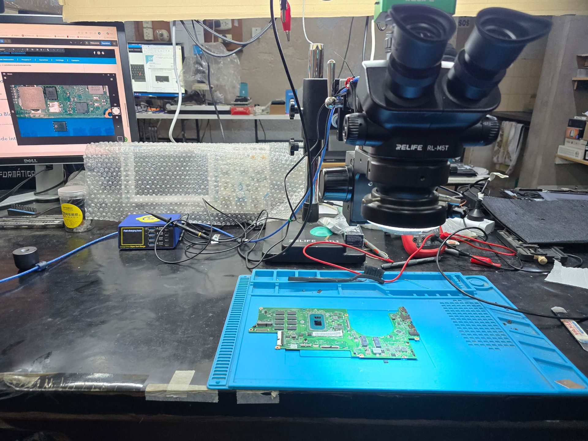 Microsoldadura de motherboard de notebook en laboratorio técnico de CM Informática en Bahía Blanca, con microscopio y componente ampliado en pantalla Dell.