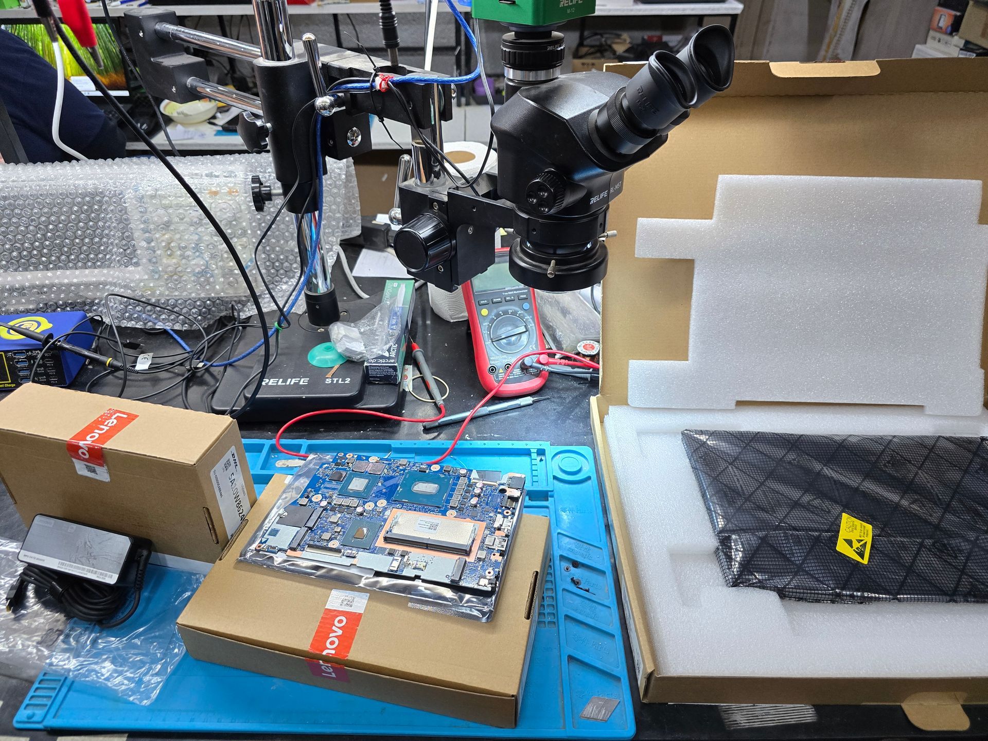 Cargador, motherboard y pantalla Lenovo originales sobre cajas oficiales en el laboratorio técnico de CM Informática Bahía Blanca