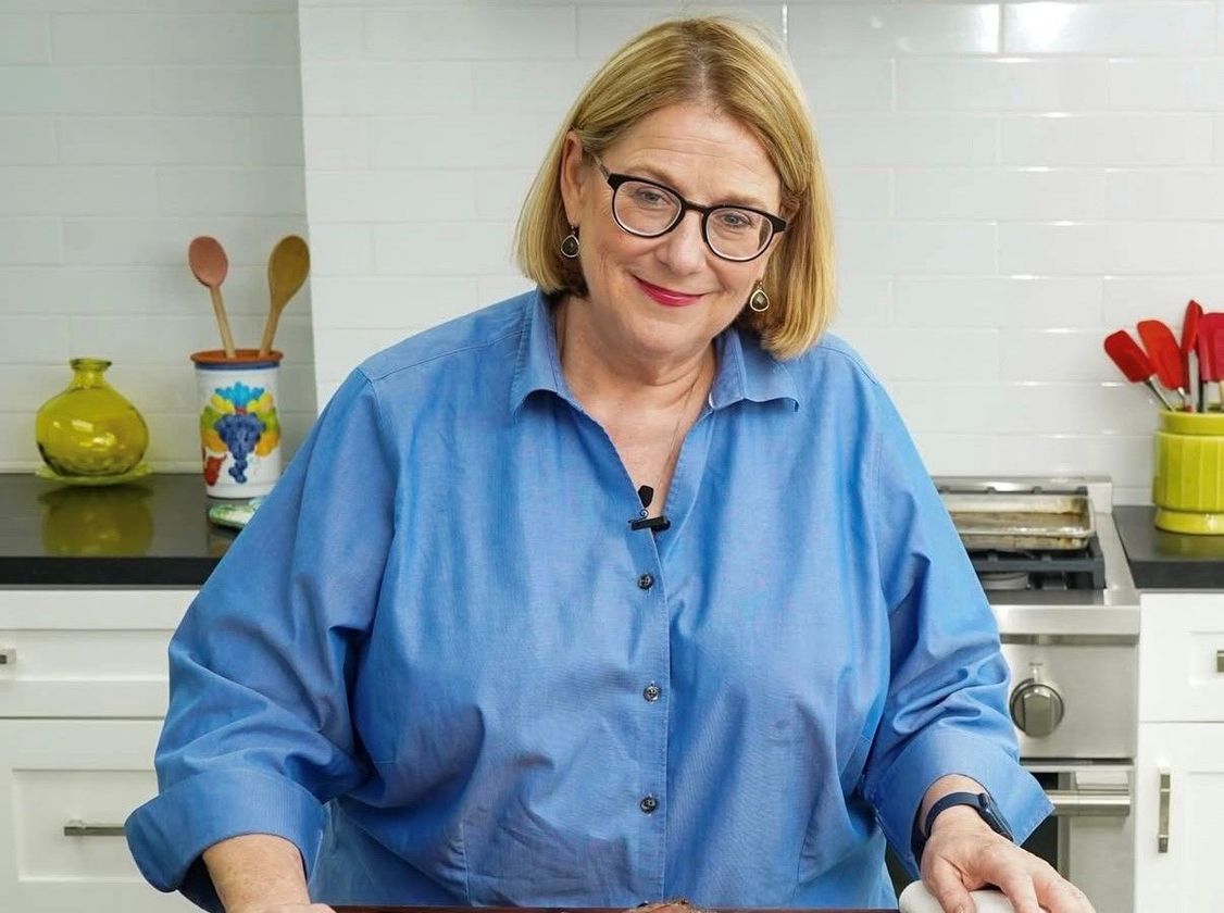A woman wearing glasses and a blue shirt is standing in a kitchen.