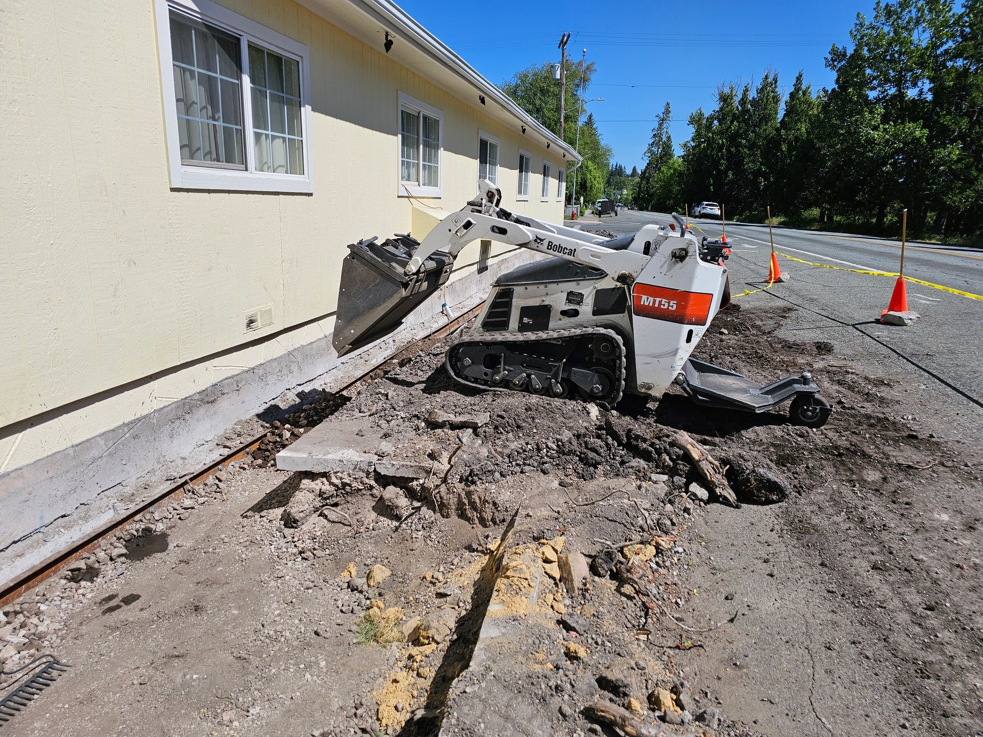 A skidsteer is working on a sidewalk next to a house getting foundation repair in Medford, Oregon