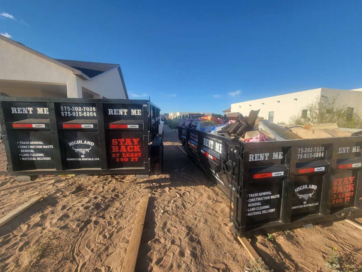 A couple of dumpsters are sitting in the dirt in front of a house