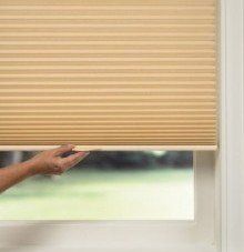 A person is opening a honeycomb blind on a window.