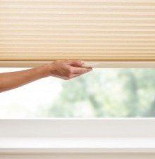 A person is opening a honeycomb blind on a window.