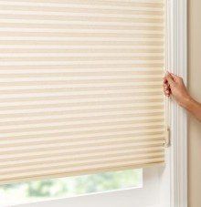 A person is opening a honeycomb blind on a window.