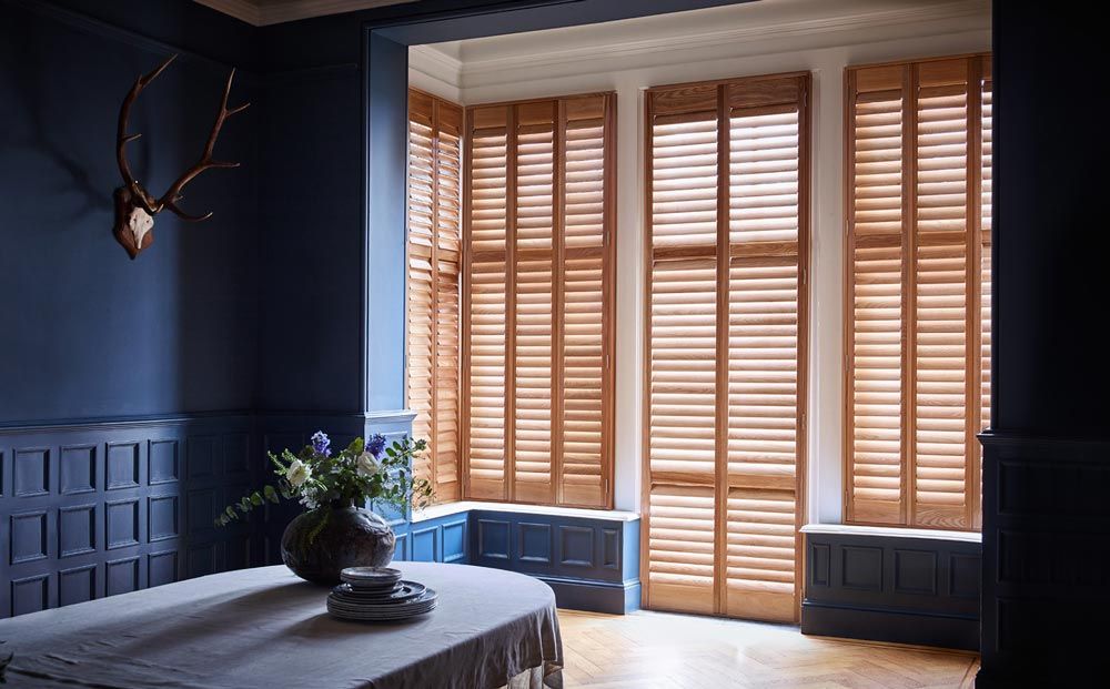 A dining room with a table and shutters on the windows.