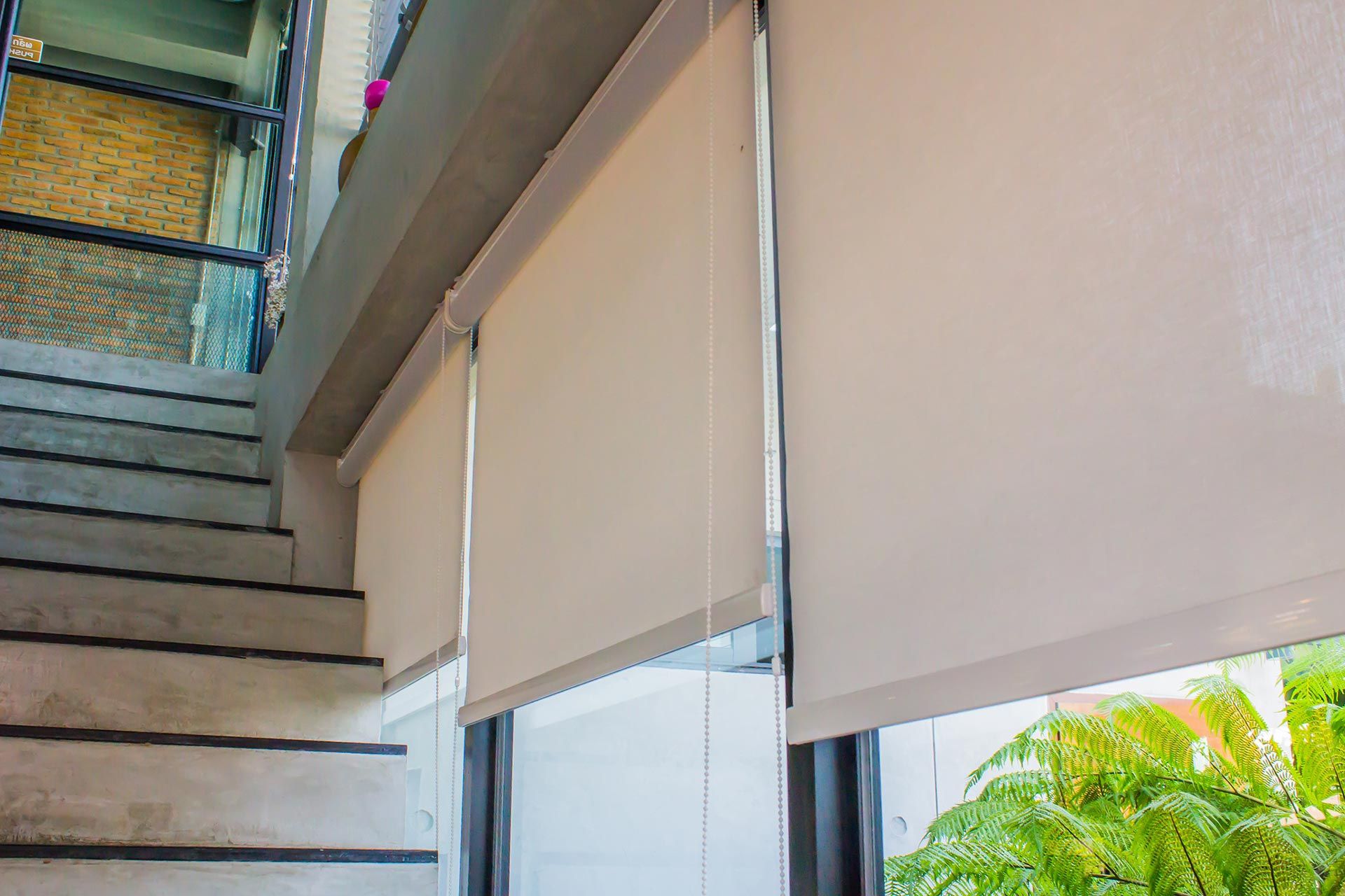 A pair of roller blinds hanging on a window next to a set of stairs.
