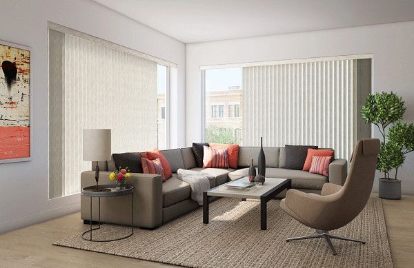 A living room with a large couch and large windows with vertical blinds