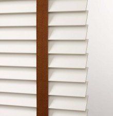 a close up of a solid & decorative tape white blind with a brown trim on a window .