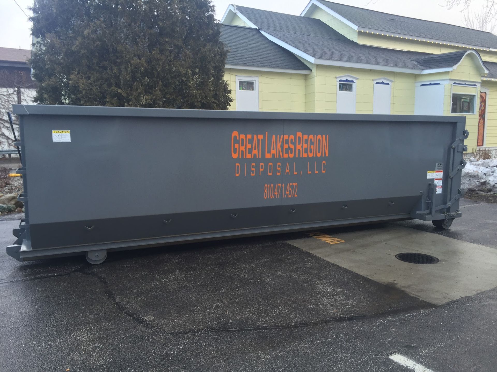 A gray roll-off dumpster from Great Lakes Region Disposal LLC parked on a paved lot in front of a yellow building.