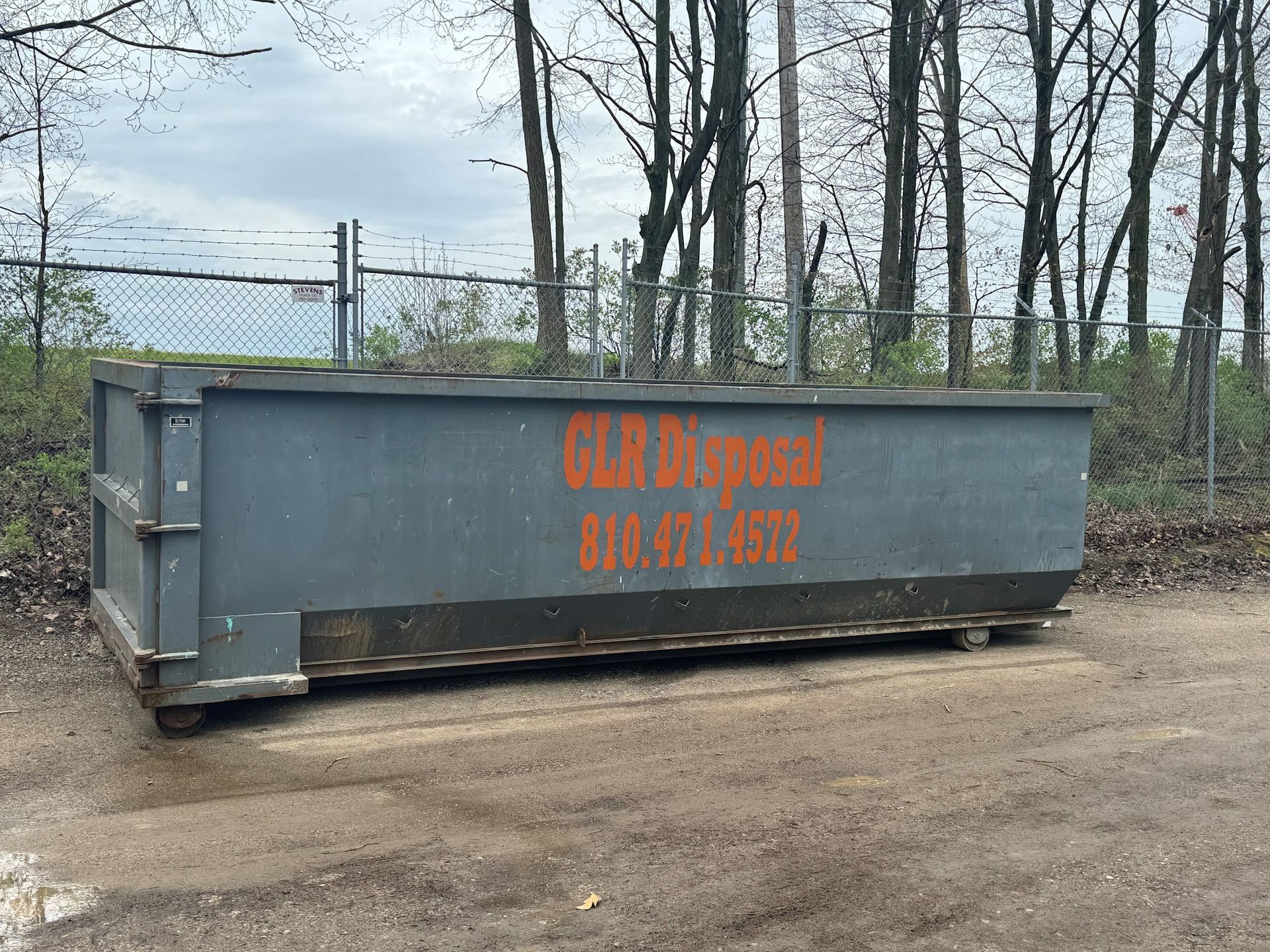 A large, grey industrial dumpster with orange text reading 
