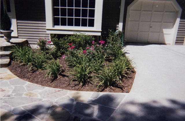 A flower bed in front of a house with a garage door