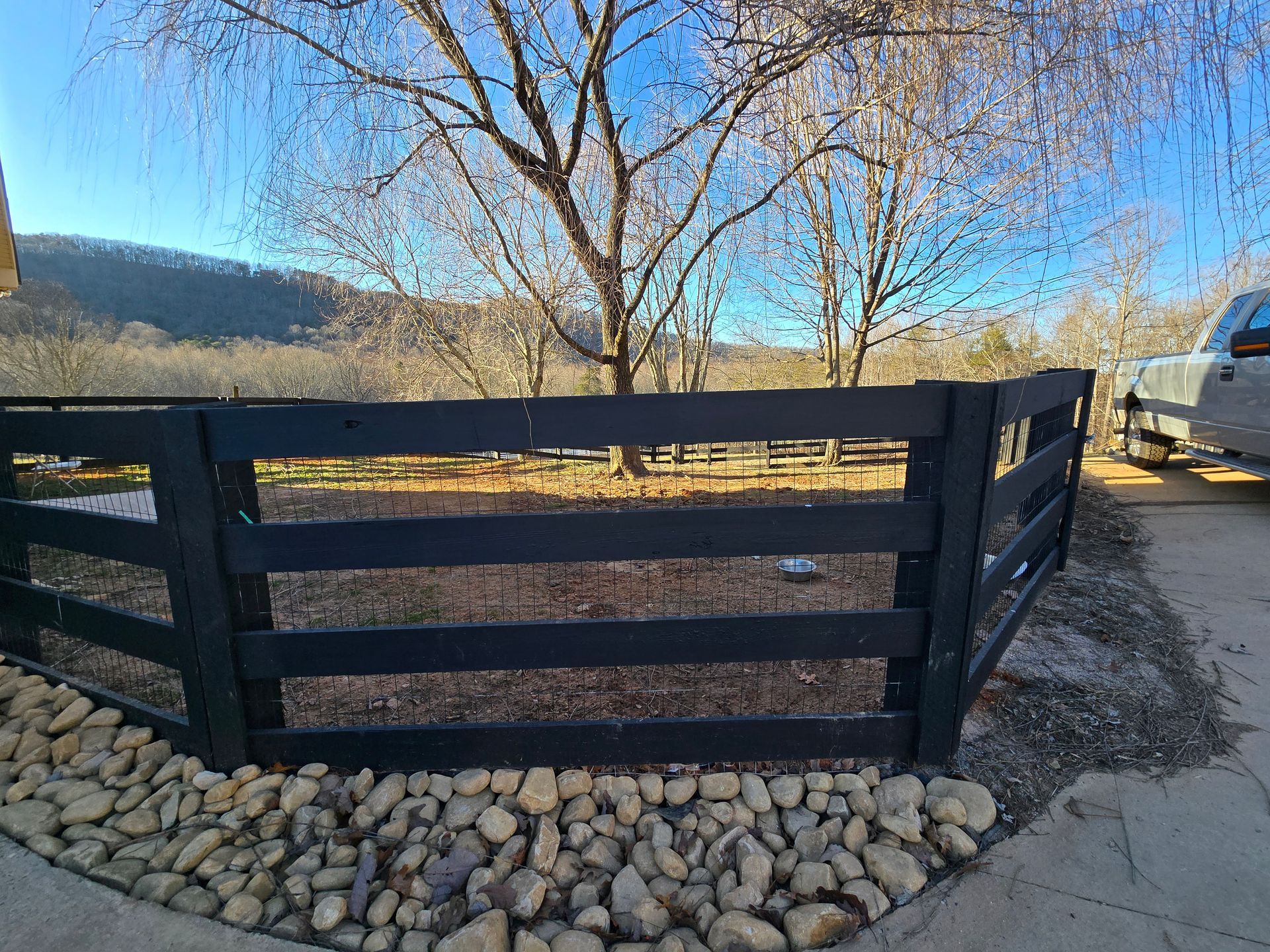 A black wooden fence is surrounded by rocks and trees.