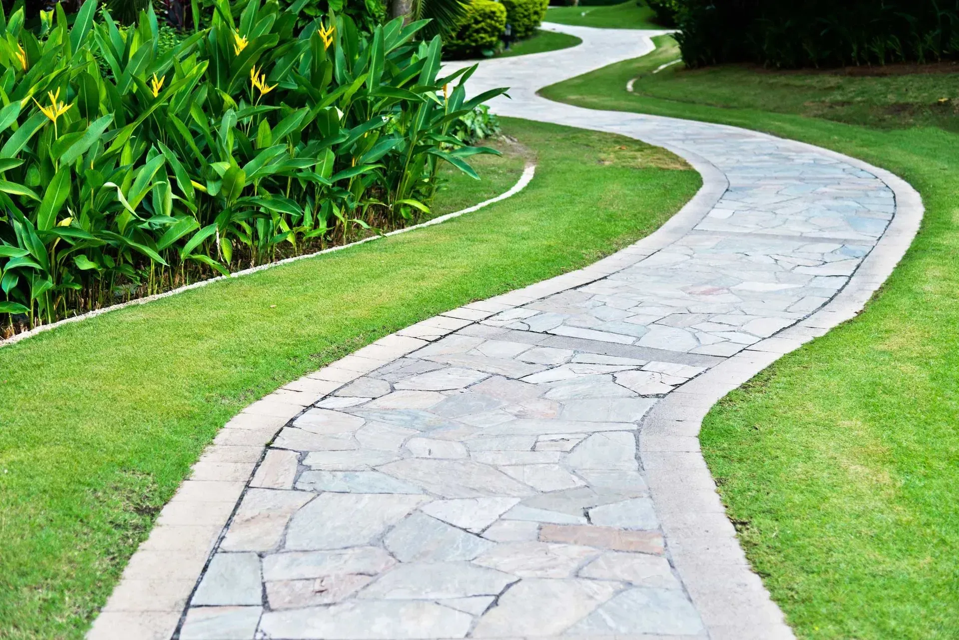A stone walkway winds through a lush green park.