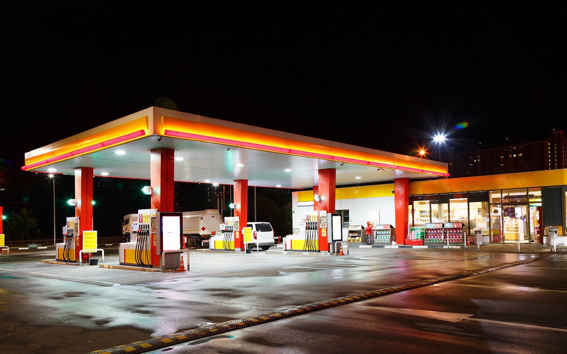 Shell gas station at night, brightly lit, with cars and a convenience store.
