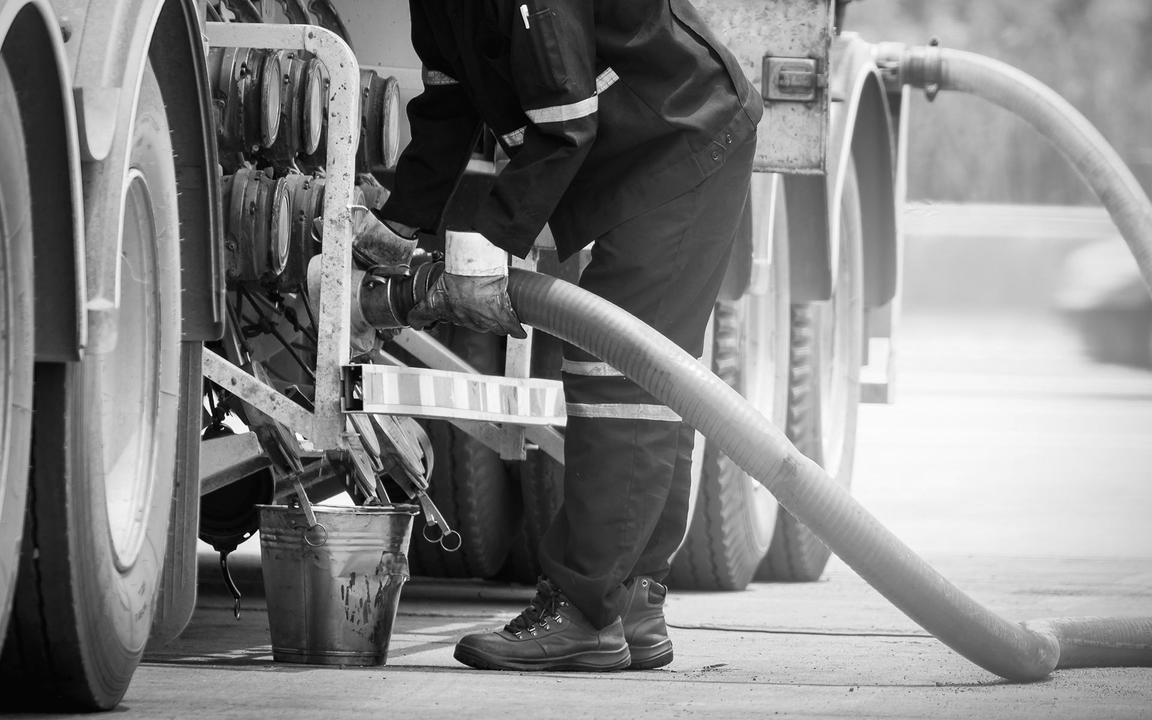 Firefighter connects hose to a tanker truck. Black and white image.