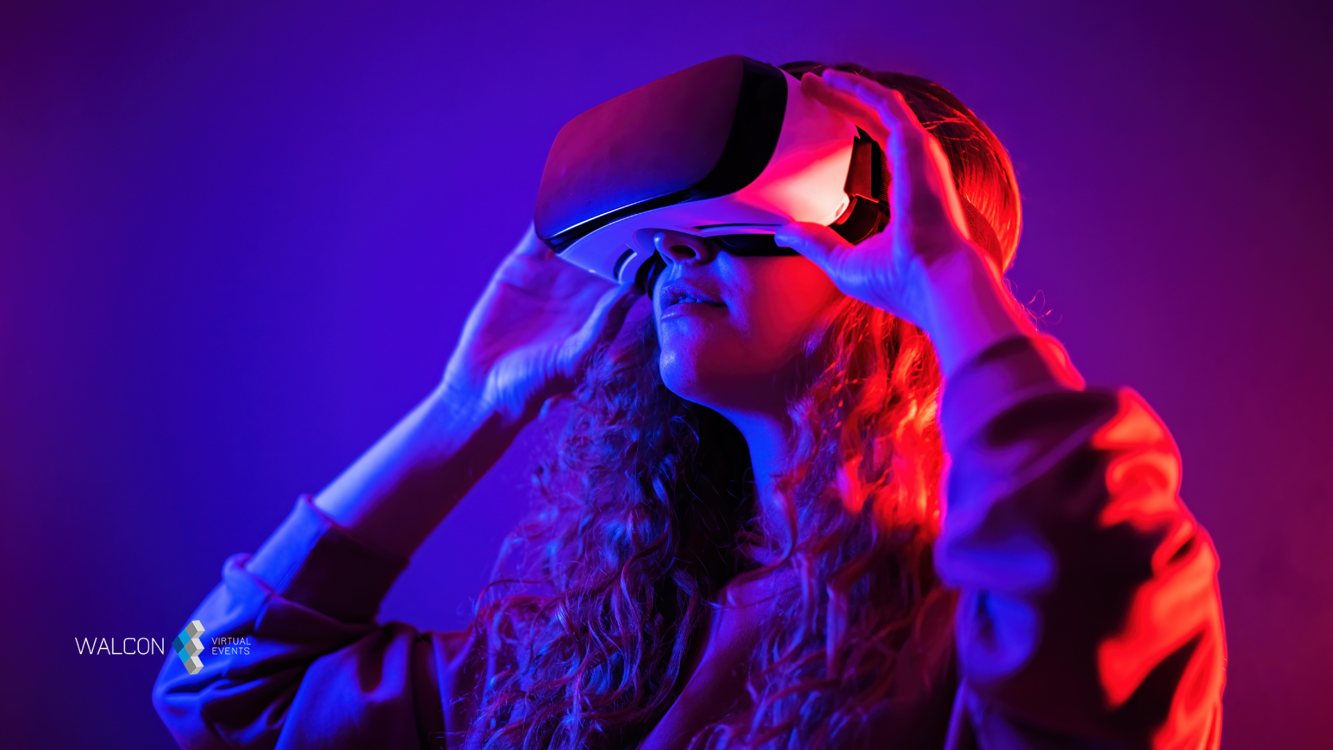 Woman adjusting VR headset, illuminated by red and blue light.