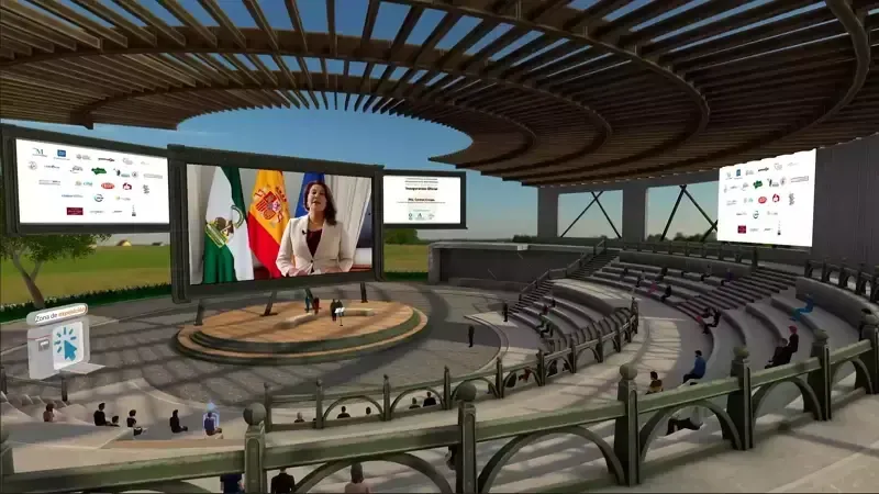 Virtual conference: woman on screen, Spain flag backdrop, circular stage, audience in bleachers.