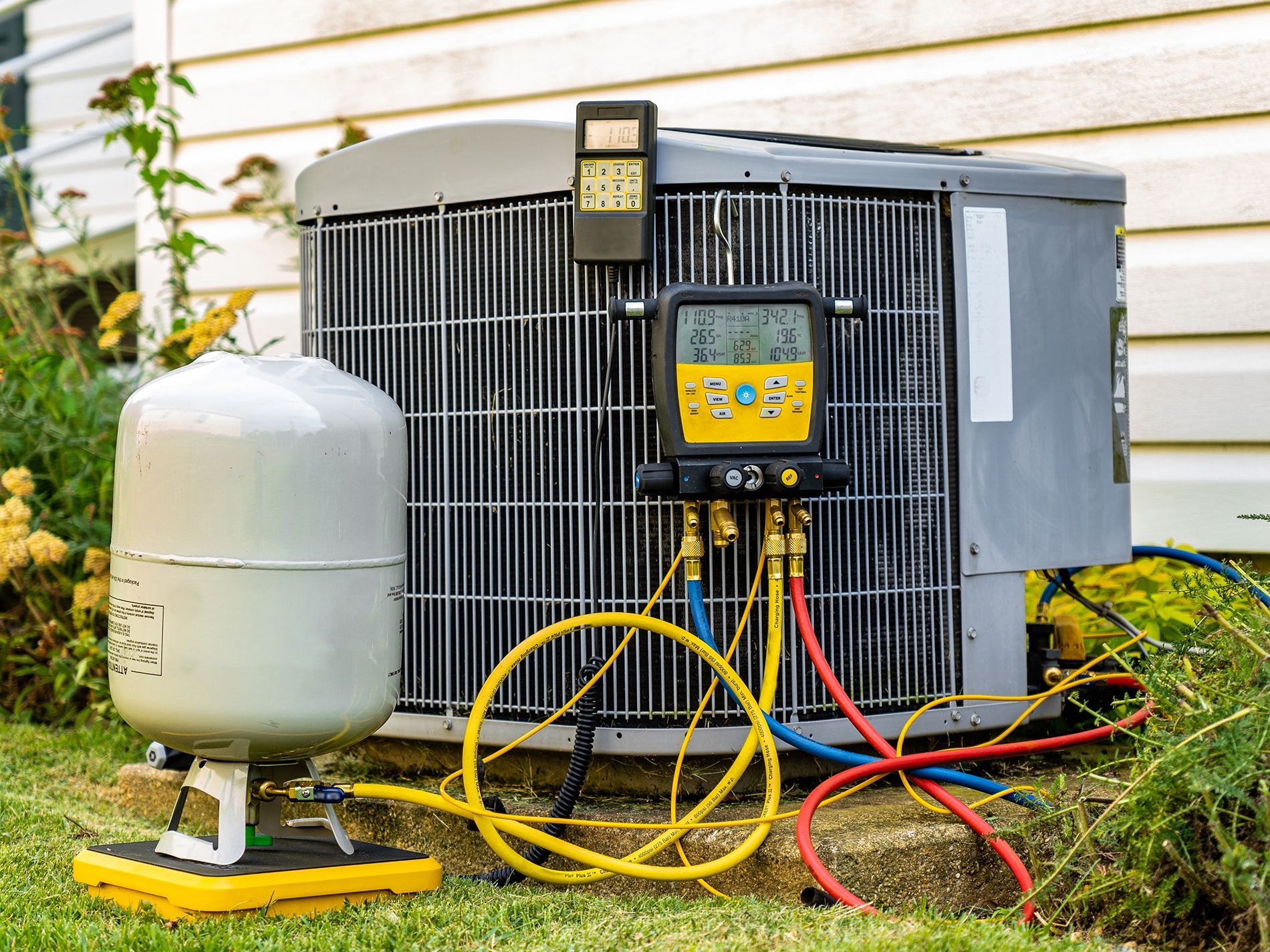 HVAC unit with gauges connected, outdoors near a house, being serviced.