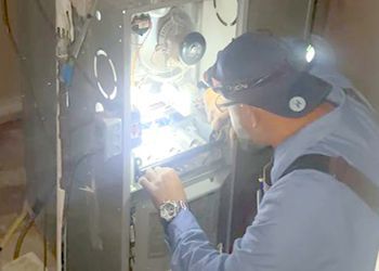 A man is working on an air conditioner with a flashlight.