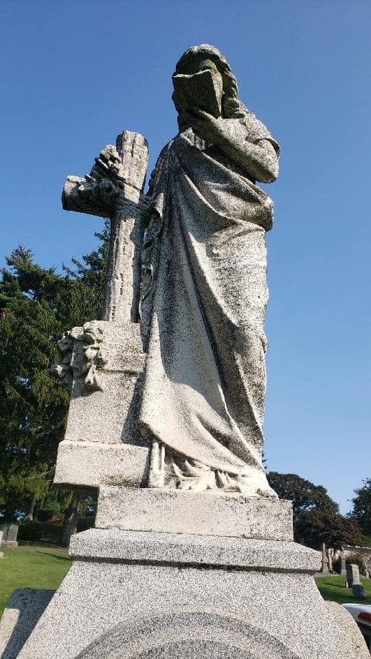 a statue of a woman holding a cross in a cemetery .
