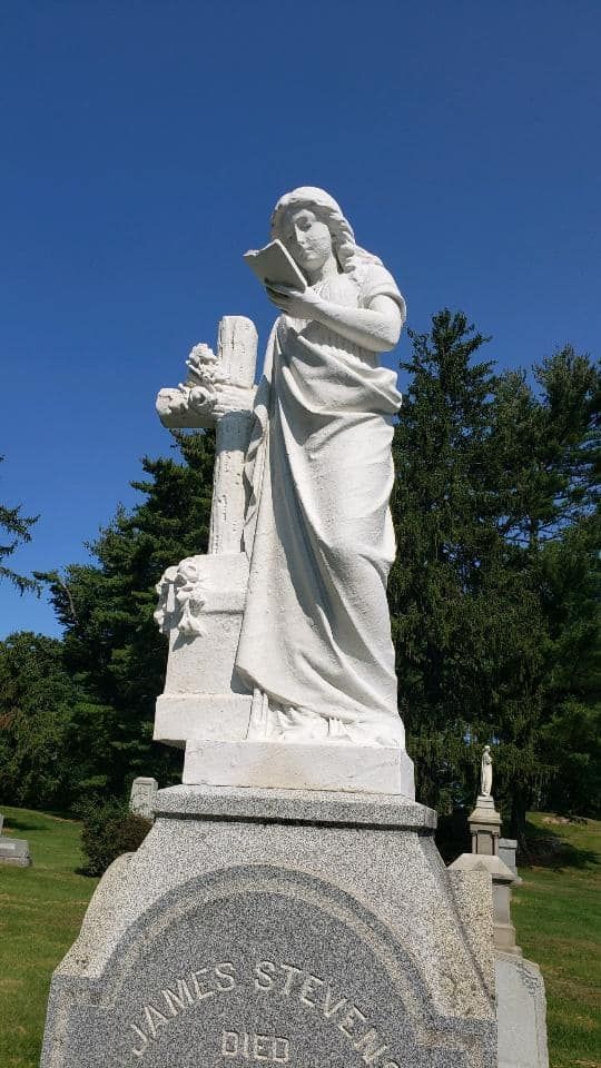 a statue of a woman holding a book in a cemetery .