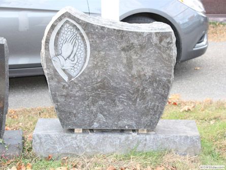 a gravestone with a praying hand on it is in front of a car .