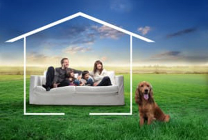 A family is sitting on a couch in a field with a dog.