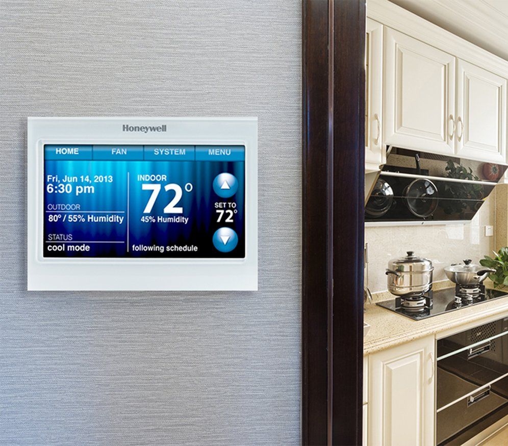 A honeywell thermostat is mounted on a wall next to a kitchen.