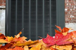 A close up of a air conditioner surrounded by autumn leaves.