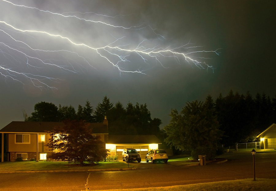 Lightning strikes over a house and garage at night.