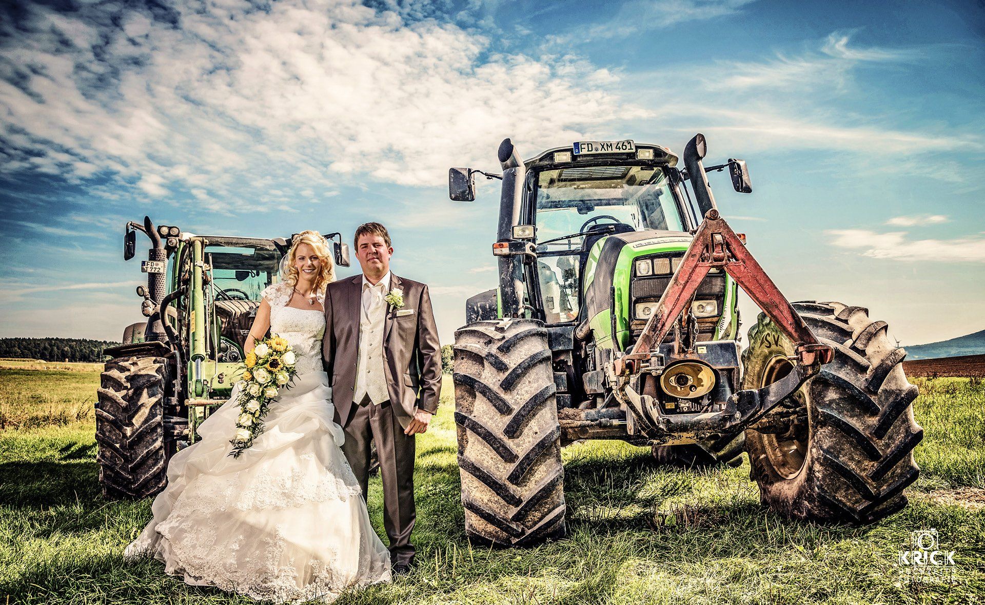 Braut und Bräutigam posieren vor zwei Traktoren für ein Foto.