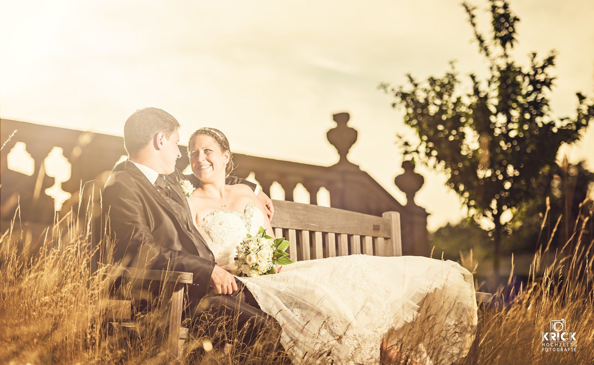 Eine Braut und ein Bräutigam sitzen auf einer Bank auf einem Feld.