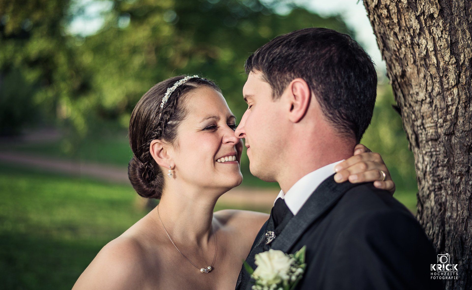 Braut und Bräutigam küssen sich vor einem Baum
