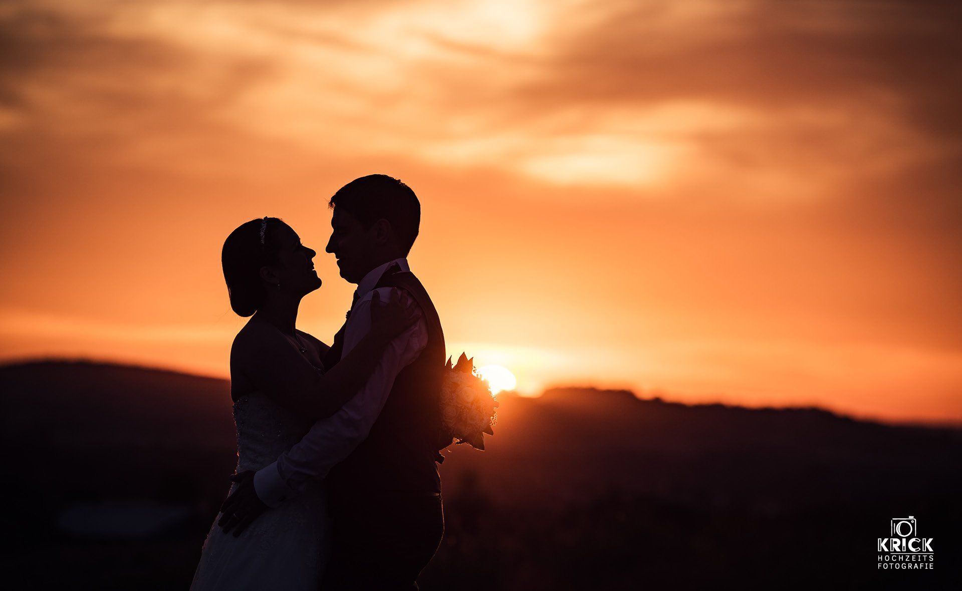 Eine Braut und ein Bräutigam stehen vor einem Sonnenuntergang.